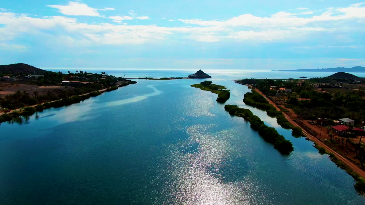 Mulege, Baja California Sur aerial view with blue-green water in the foreground, thin island vegetation dividing the channel, coastal land and small buildings to the sides, and no visible people.