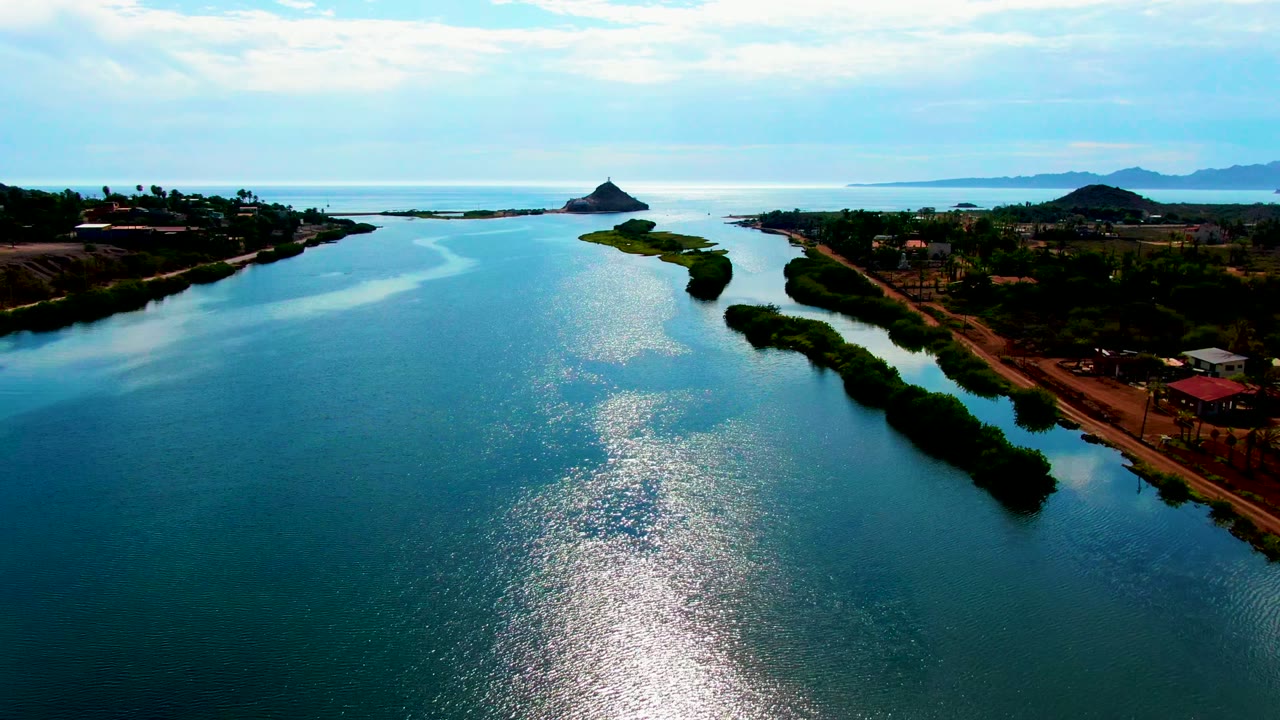 Wide aerial view of a water channel with a road and structures along the right bank.