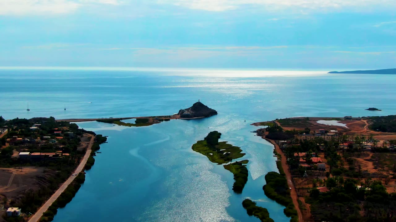 Aerial frame over Mulege, Baja California Sur showing blue water, shoreline roads, small green islands, distant land on the horizon, and no visible people.