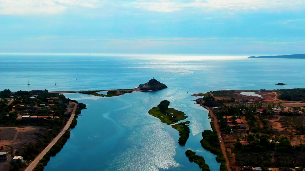 Coastal waterway with road, island vegetation, offshore rock, and bright water reflection.