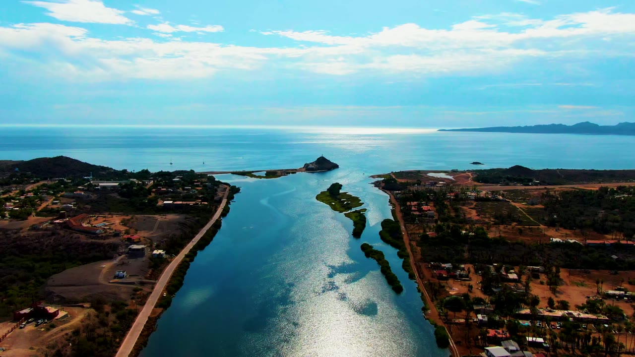 Sunlight glints on a narrow coastal waterway with land and road on both sides.