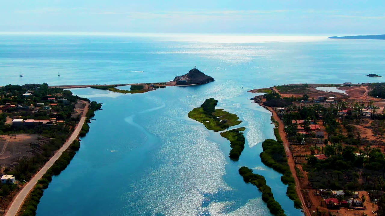 Aerial view along the channel with green strips in the water and a rocky islet offshore.