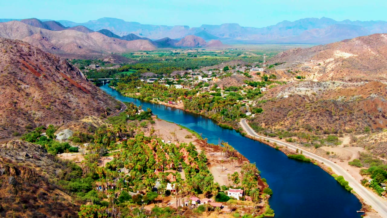Blue river curving through a valley with road and hills.