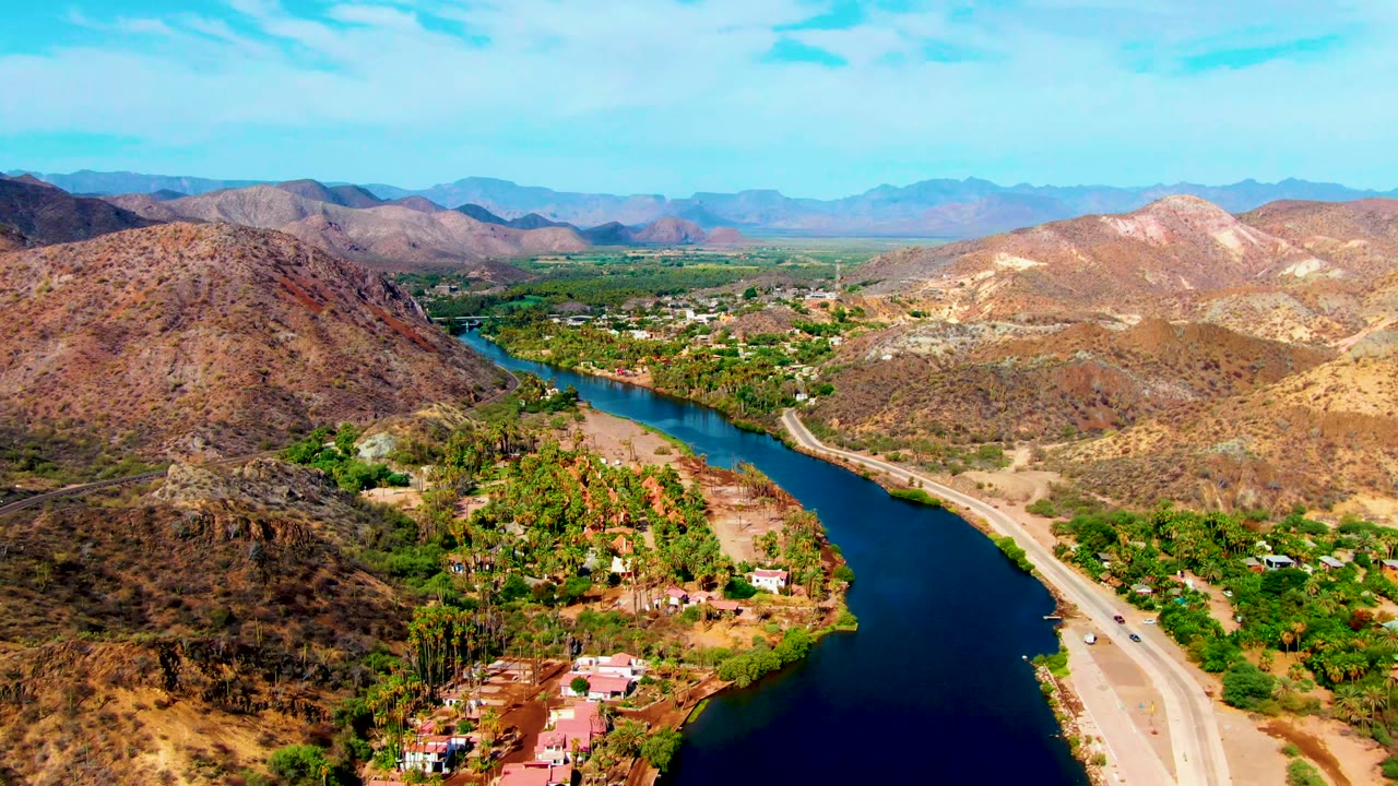 Aerial river bend with road, vehicles, desert hills, and valley settlement.