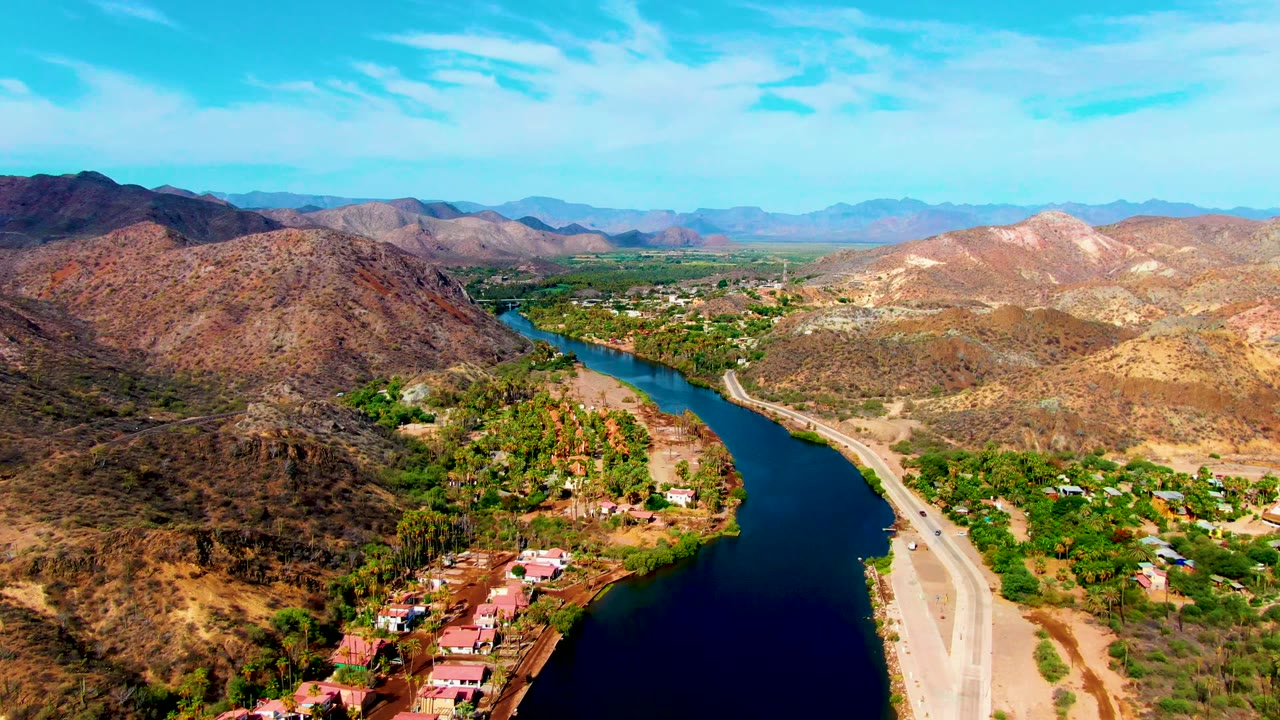 River valley with road, buildings, trees, and mountains.