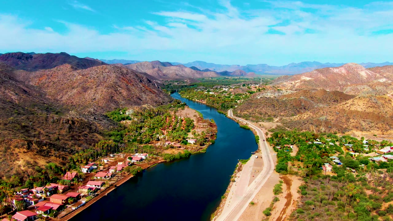 Wide aerial view of a winding river with a road and desert mountains.