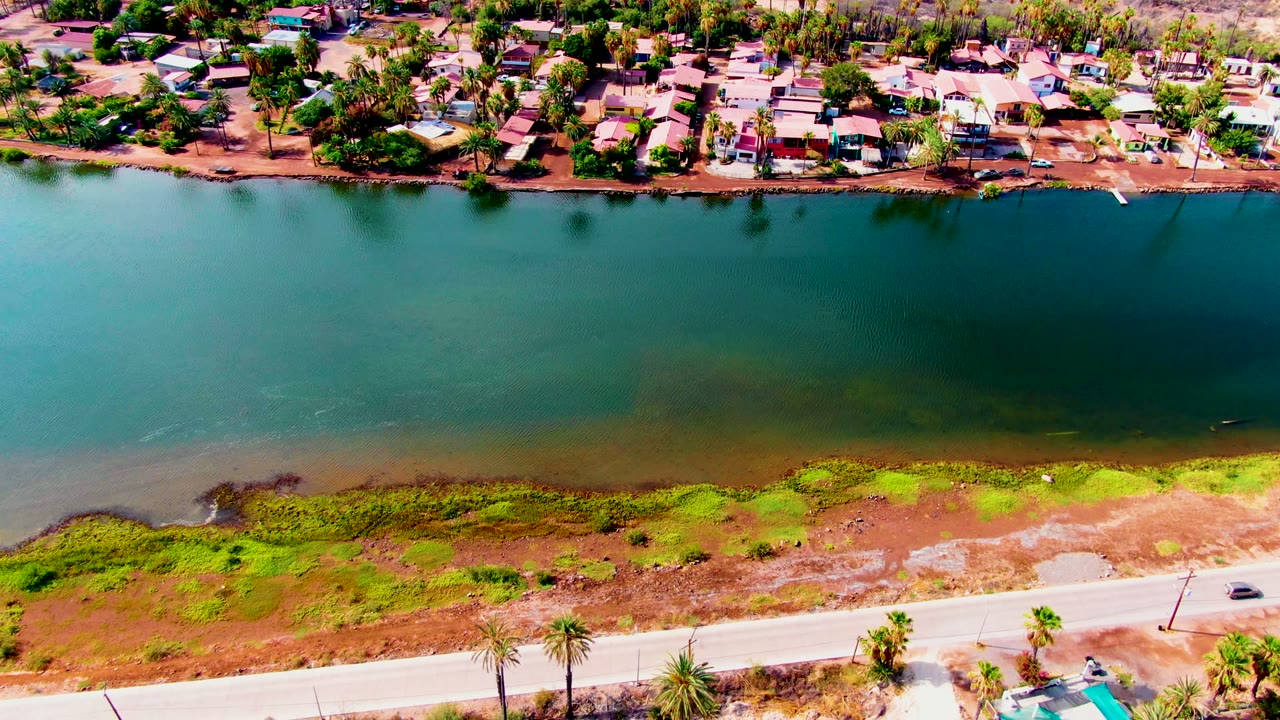 Aerial view of canal and neighborhood with the near road partly visible at the bottom.