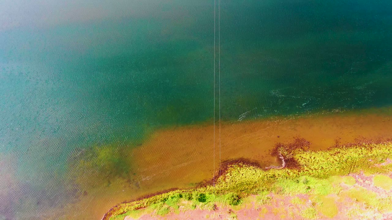 Aerial shoreline with teal water above a widening brown muddy beach.