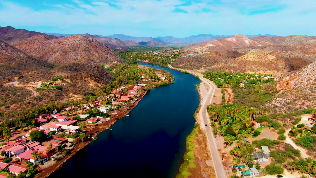 Aerial river valley with road, settlement, and arid mountains.