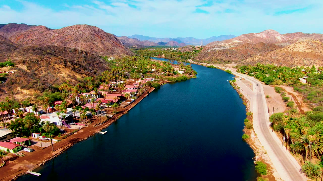 Drone view of the river curving past houses and a pale road through dry hills.