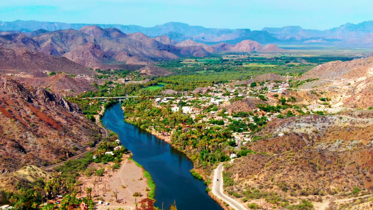 High aerial view of river, palms, road, and mountain valley town.