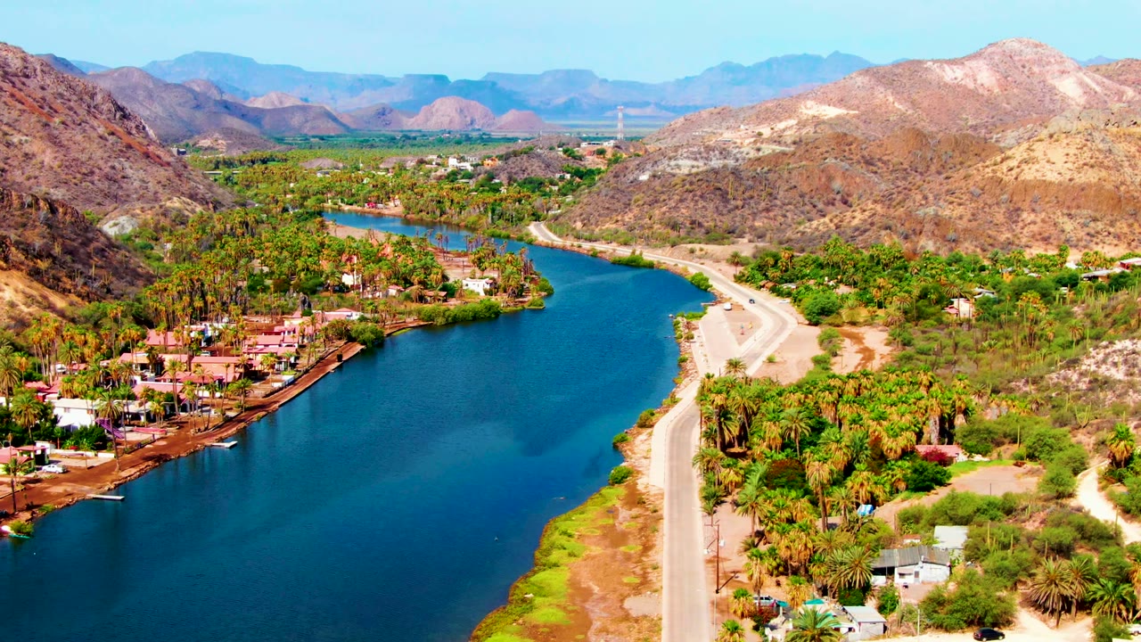 Wide aerial view of the river, road, palms, and dry mountains.