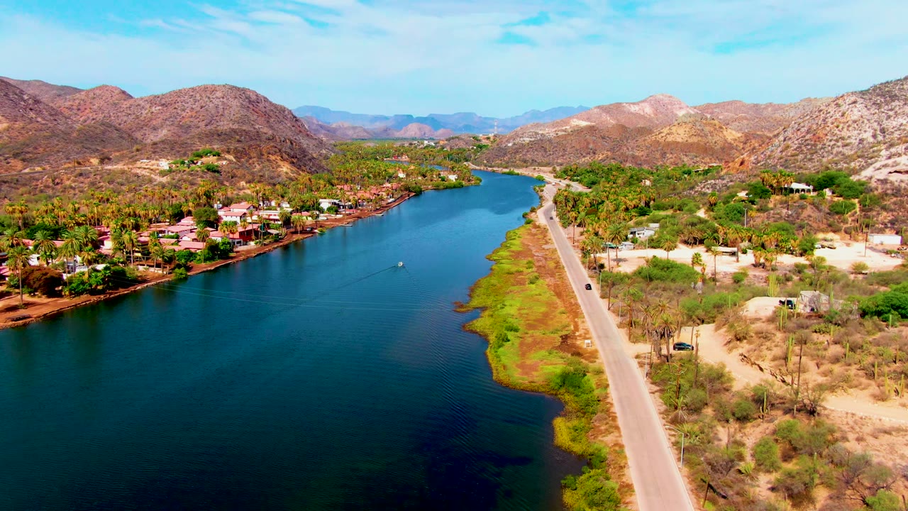 Aerial riverfront road with homes and desert hills.