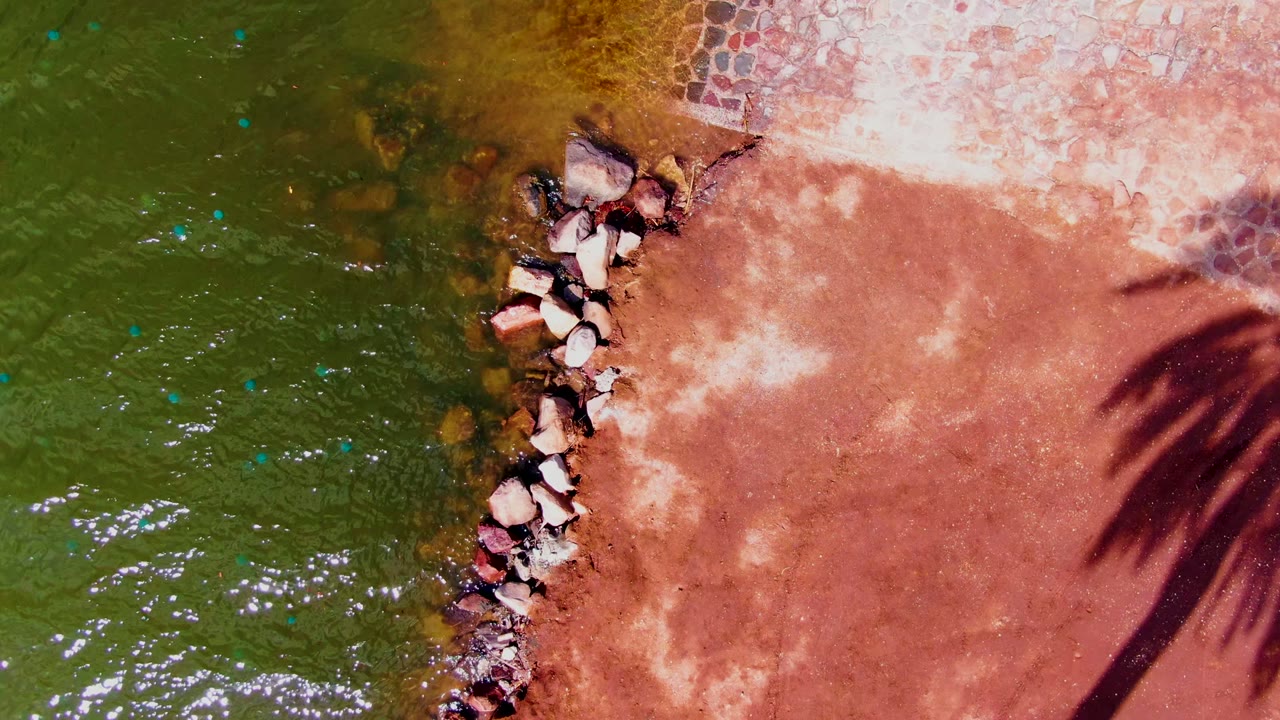 Green rippling water and diagonal rocks beside sunlit reddish shore.