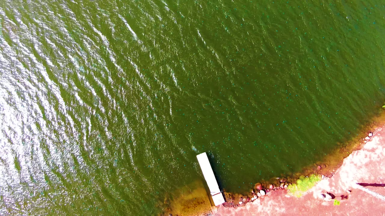 Green river surface, diagonal shore, rocks, and white dock from above.