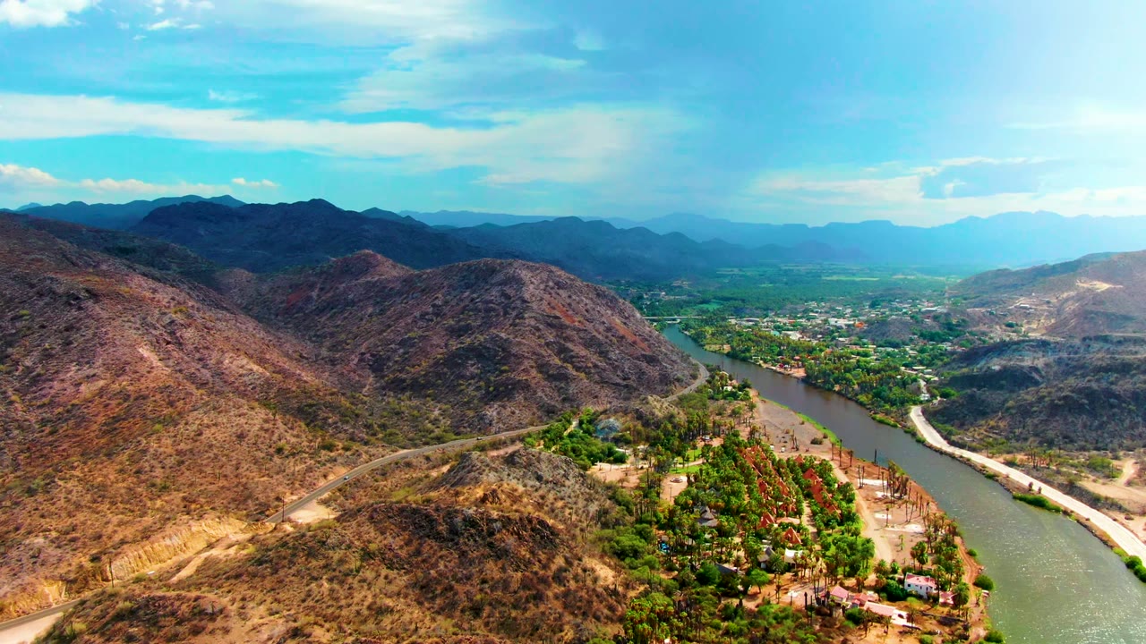 A high view over Mulege, Baja California Sur showing the river tracking diagonally through arid hills, green vegetation along the water, distant ridgelines, and no visible people.