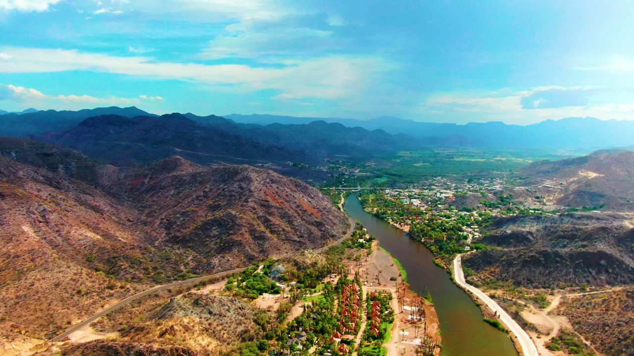 River valley with dry hills, a road, green vegetation, and distant mountains.