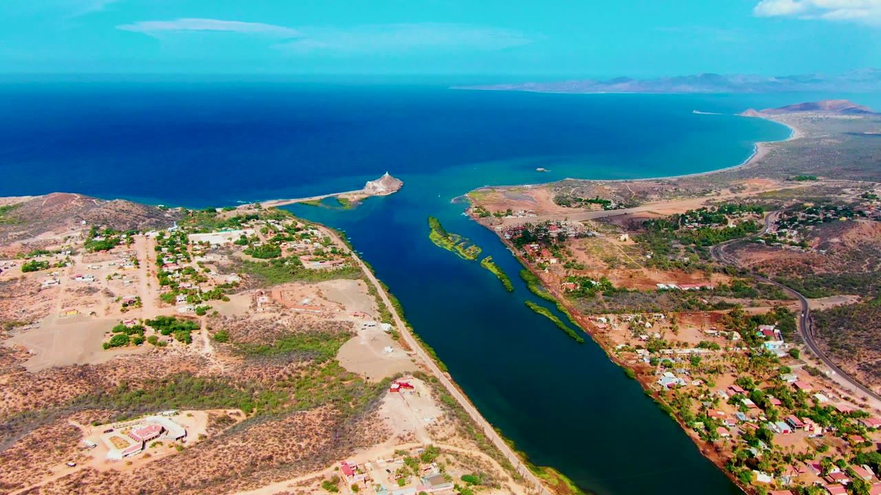 Wide drone view of coastal canal, dry land, road, and ocean.