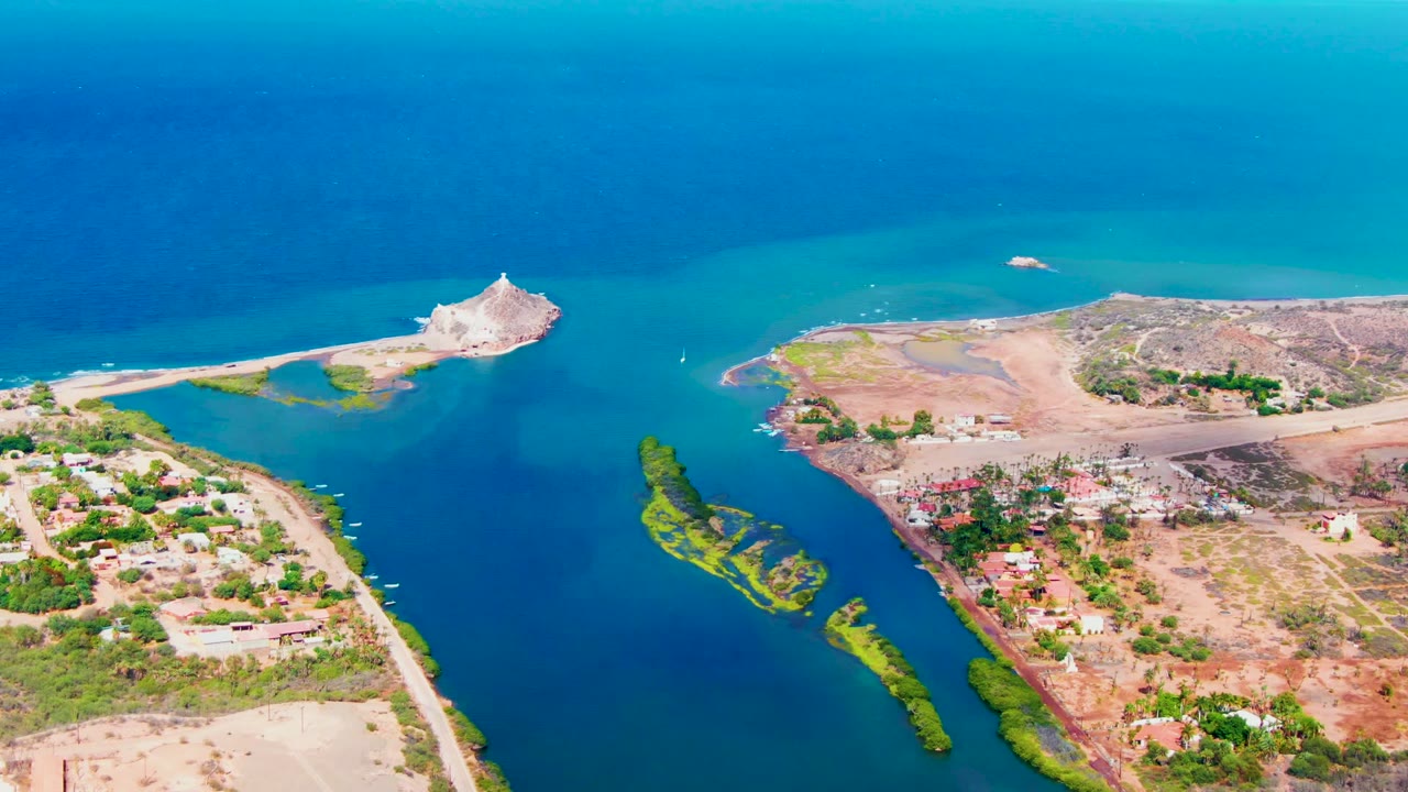 Drone view across a narrow blue waterway with island vegetation and dry settlement land.