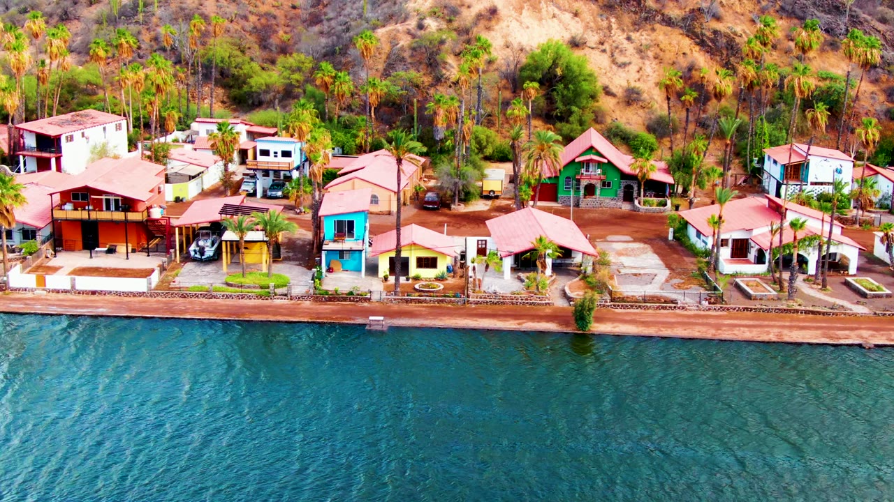 Colorful waterfront homes with red roofs, palm trees, and rippling blue water.