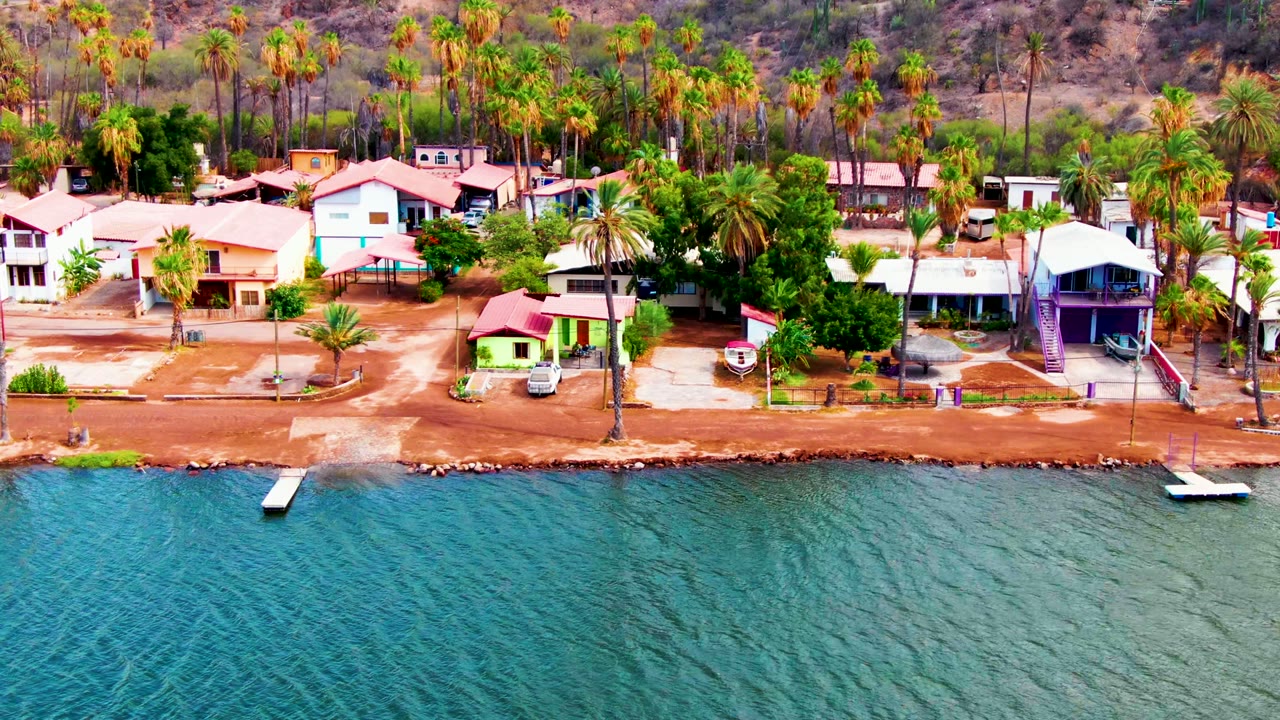 Beachfront houses and palms behind rippled turquoise water.