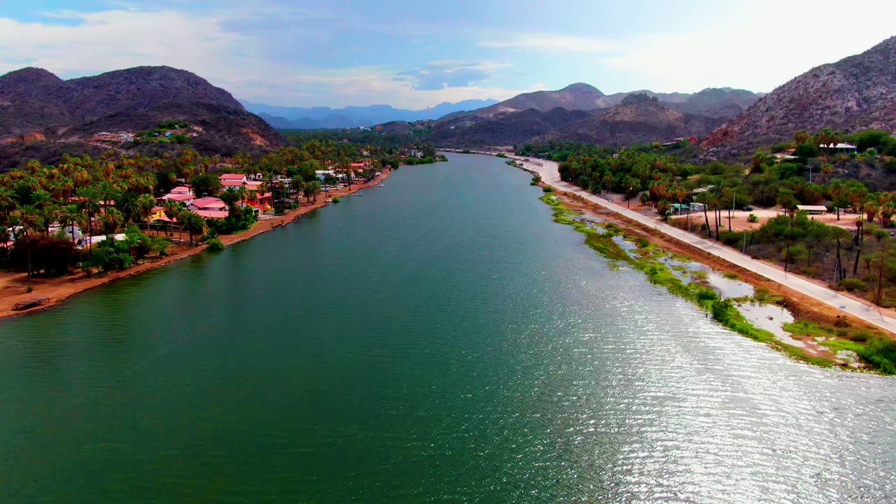 River channel with shoreline homes, road, palms, and rocky hills