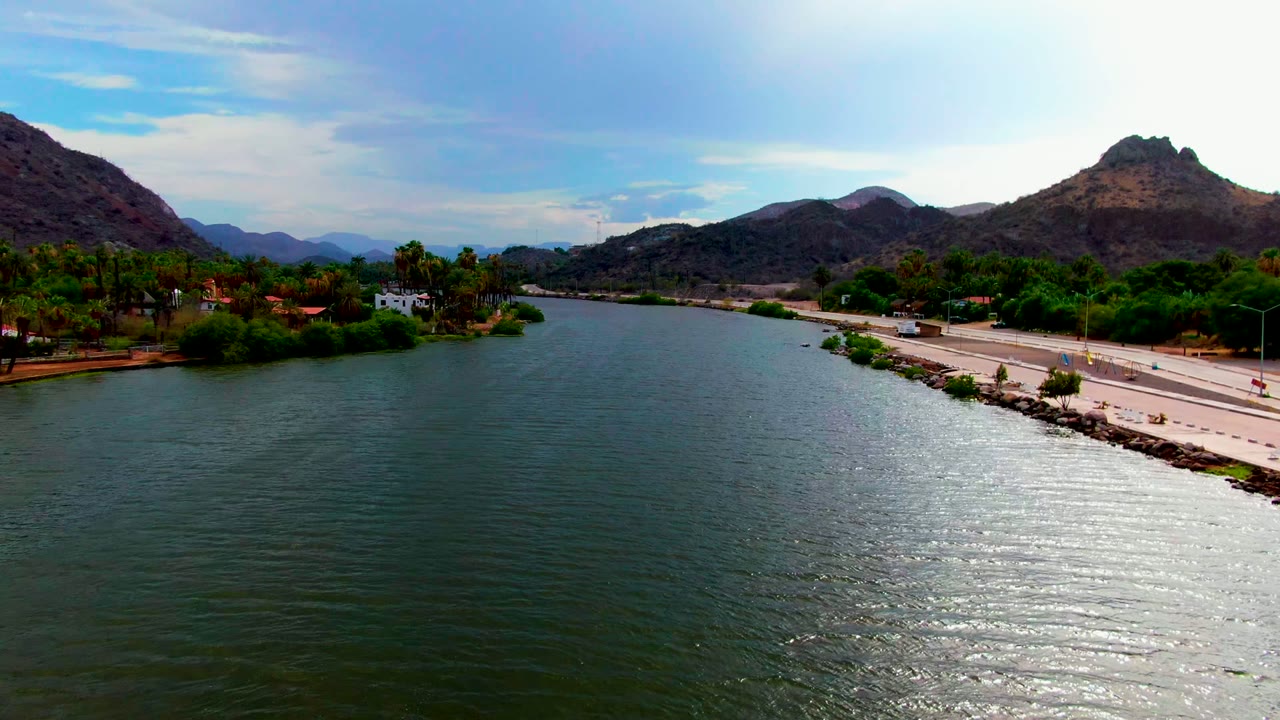 Wide aerial view over river and roadside below brown hills