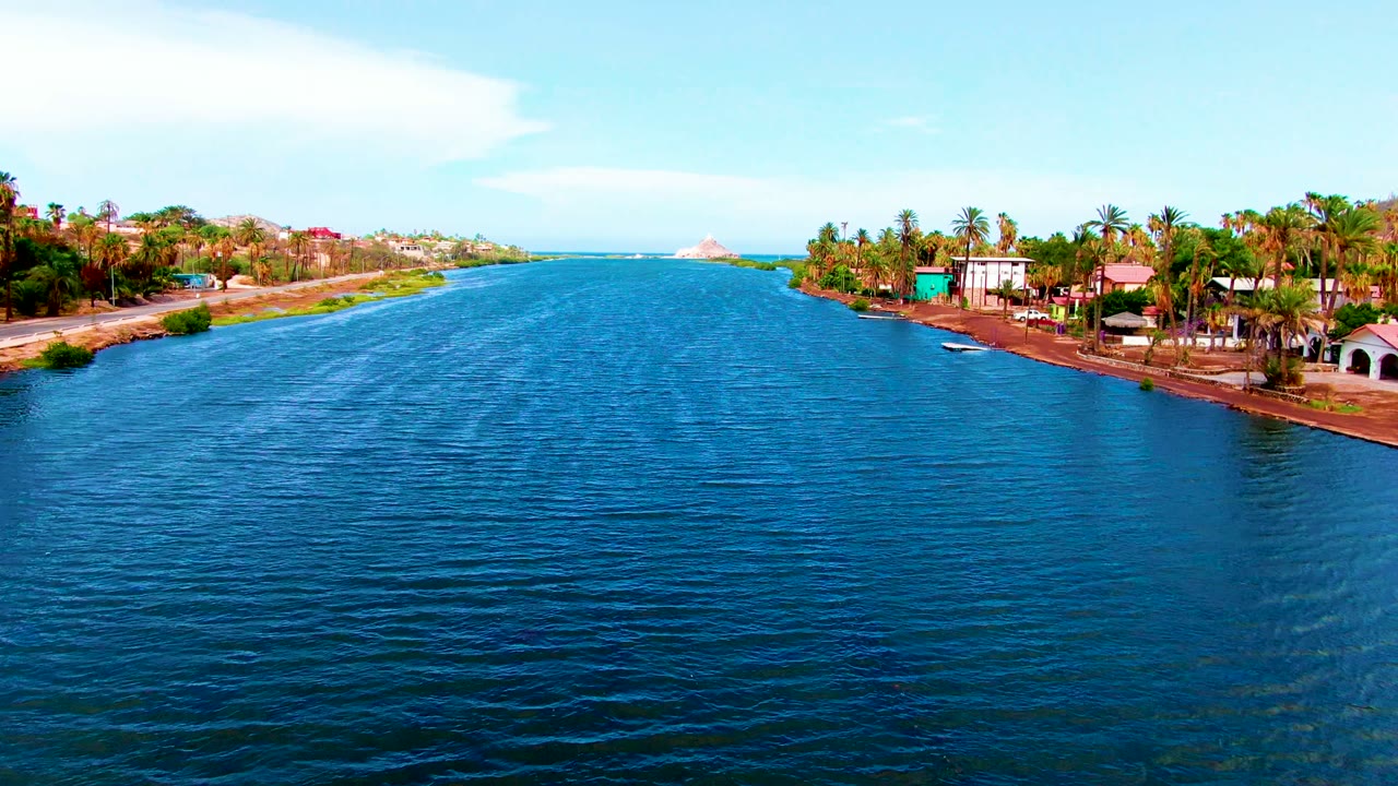 Blue waterway between palm-lined banks with homes along the right shore.