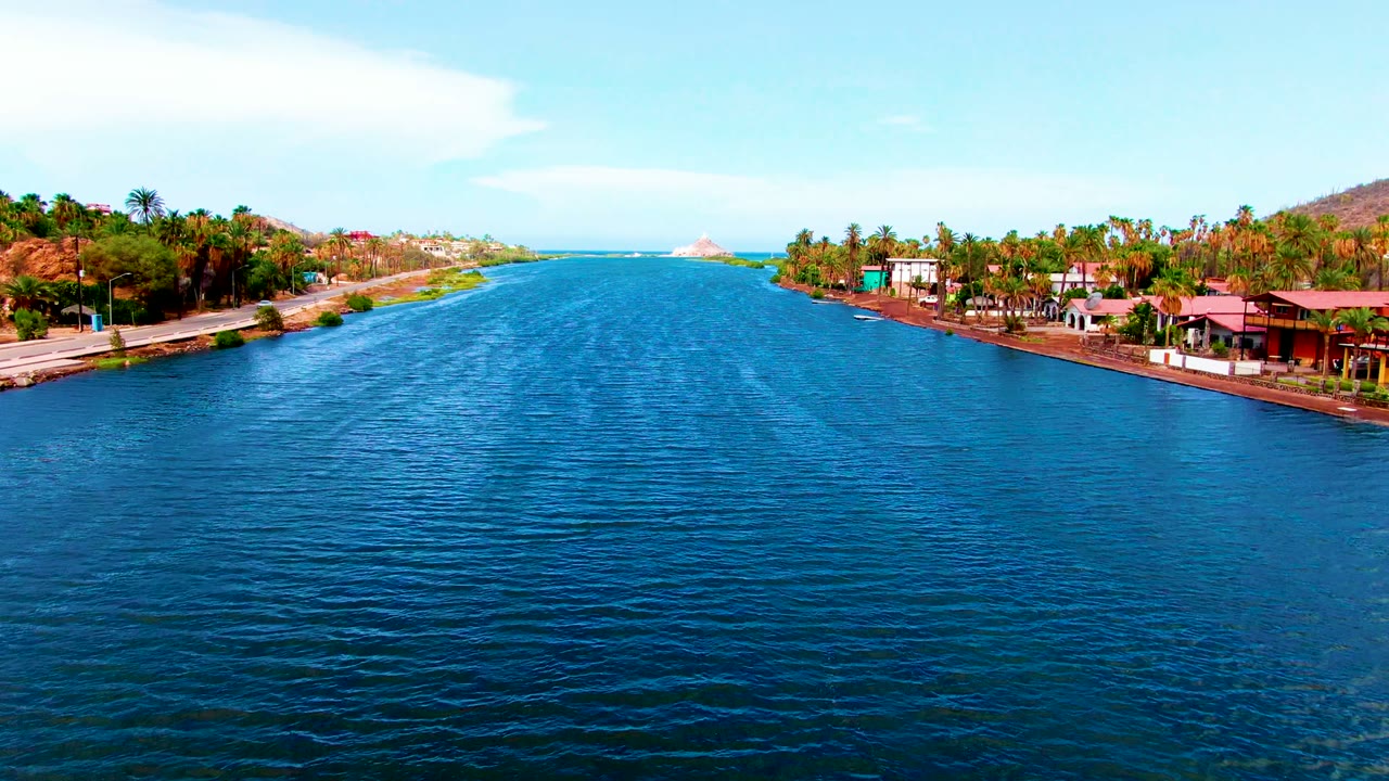 Blue canal water with palm-lined banks and waterfront buildings under clear sky