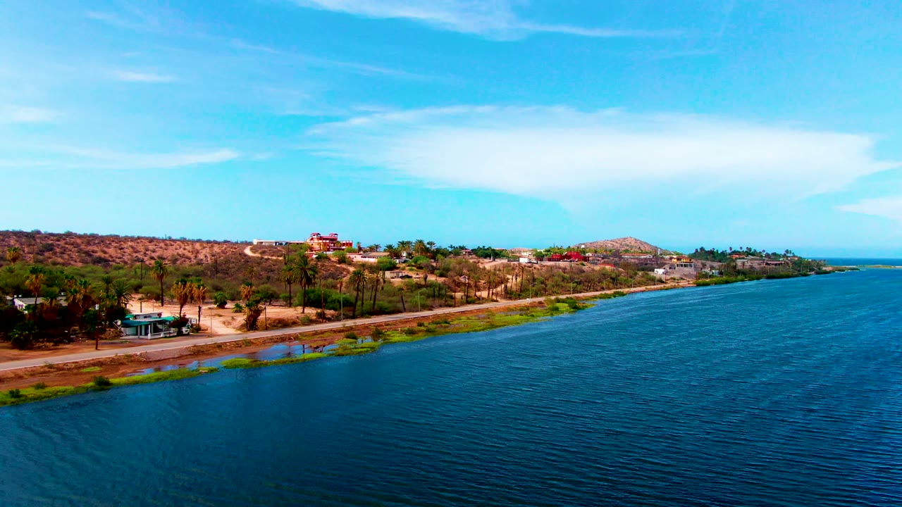 Shoreline road runs between blue water and dry hills with palms.