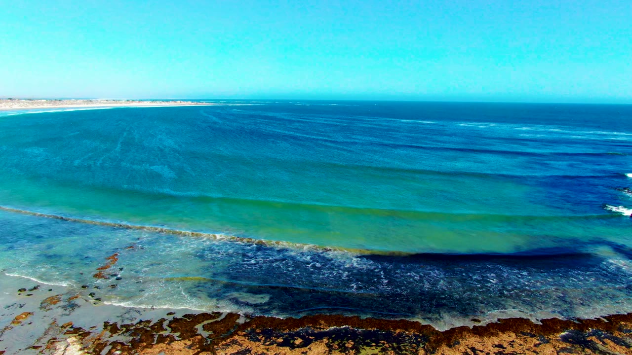 Wide aerial coastal view with blue-green water and dark seaweed bands