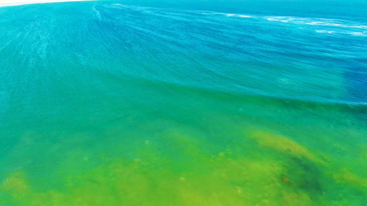 Aerial view over La Bocana shallows with yellow-green seabed color filling the lower frame, turquoise water above, faint wave lines, and no visible people.