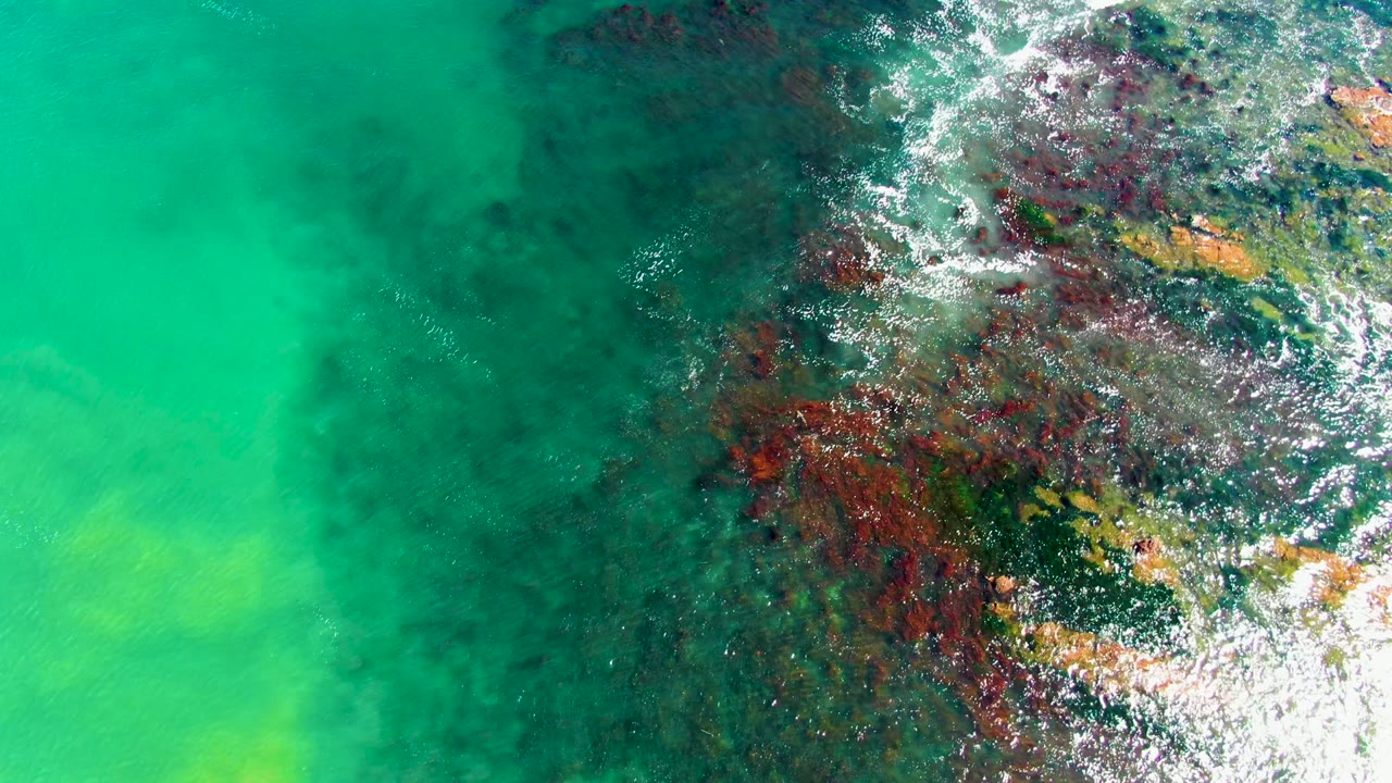 Clear green-blue water with submerged rocks and bright foam on the right