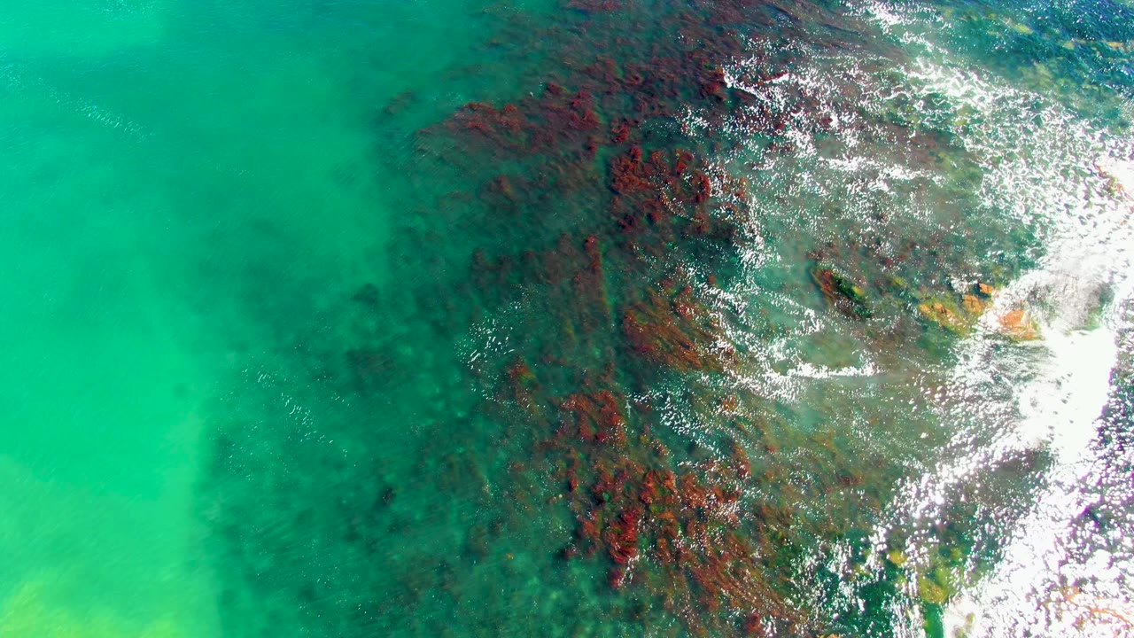 Clear green-blue water over rocky seabed with foam streaks.