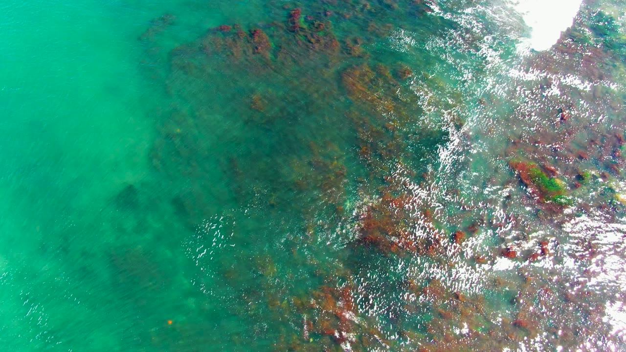 Clear green-blue water with submerged rock patches and rippled highlights.