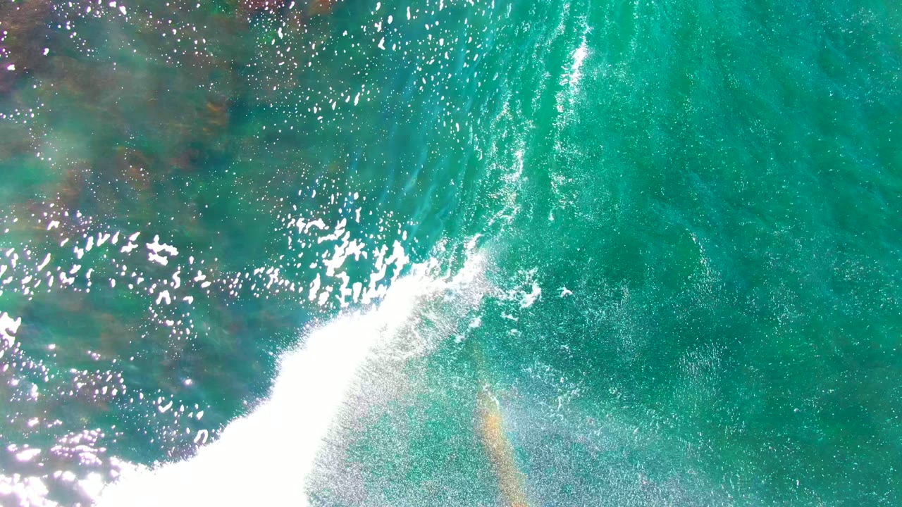 White wave foam crossing turquoise water with reef visible beneath.