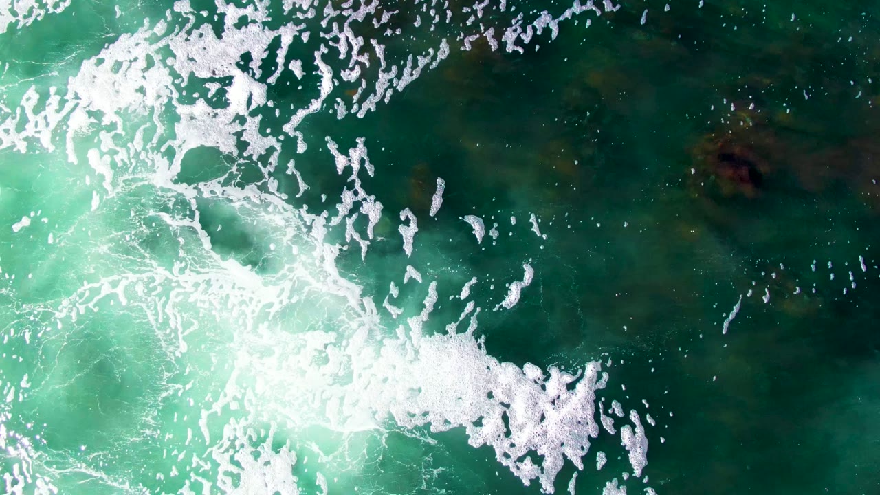 Overhead green-blue ocean surface with bright white foam patterns.