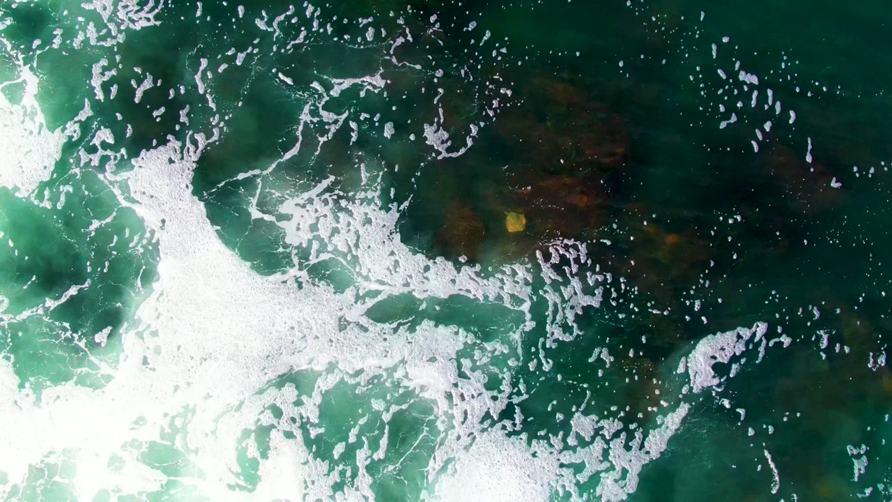 Bright foam spreading over turquoise water and rocks