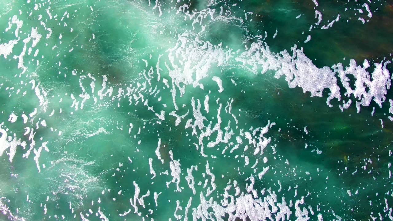 Overhead view of turquoise and dark green ocean water at La Bocana with scattered white foam streaks and no visible people.