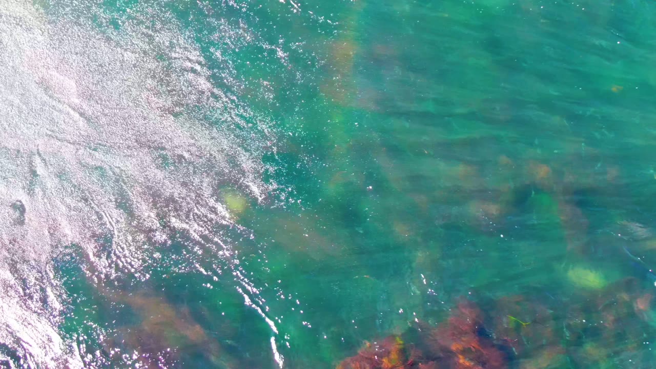 Clear green-blue water with ripples, glare, rocks, and a yellow object.