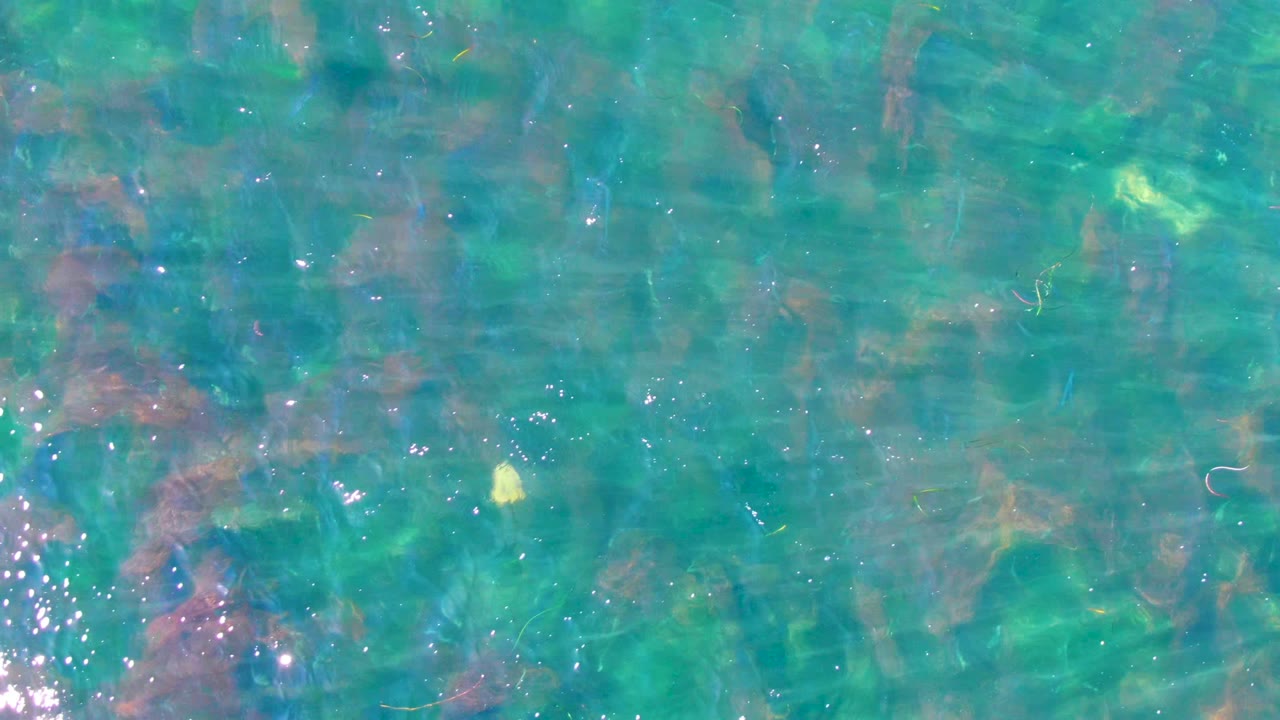 Clear shallow water at La Bocana with green-blue color, small surface ripples, submerged rocky patches, and no visible people.