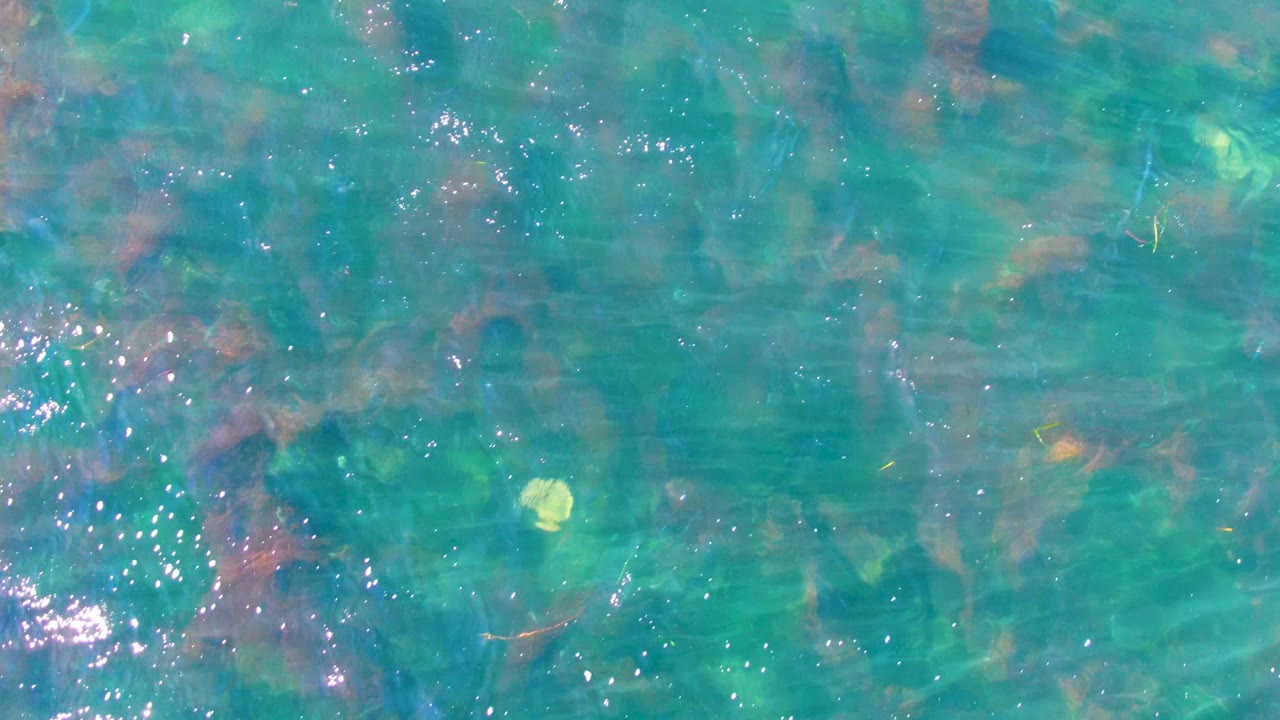 Turquoise water surface with bright glints and rocks below.
