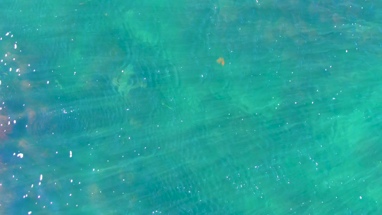 Clear turquoise water surface in La Bocana with fine ripples, faint underwater texture, scattered white sun glints, and no visible people.