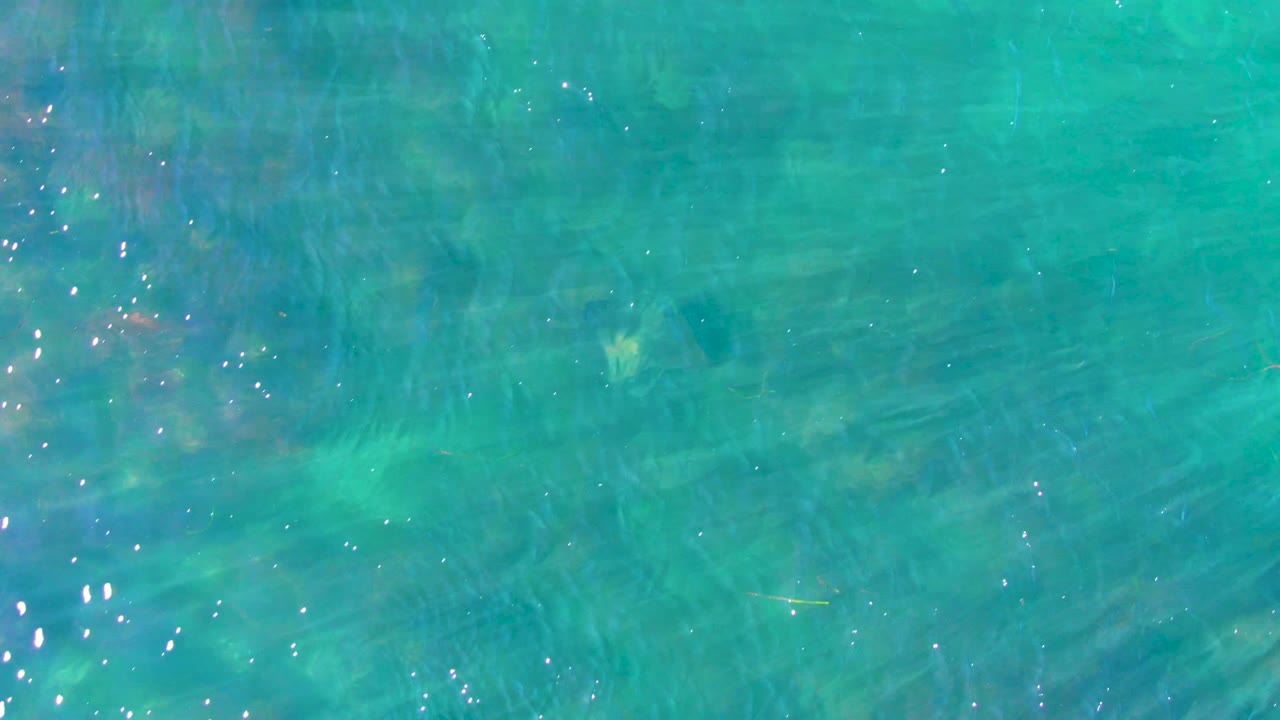 Overhead view of clear turquoise water in La Bocana, Baja California Sur, with faint ripples, visible bottom texture, and no visible people.