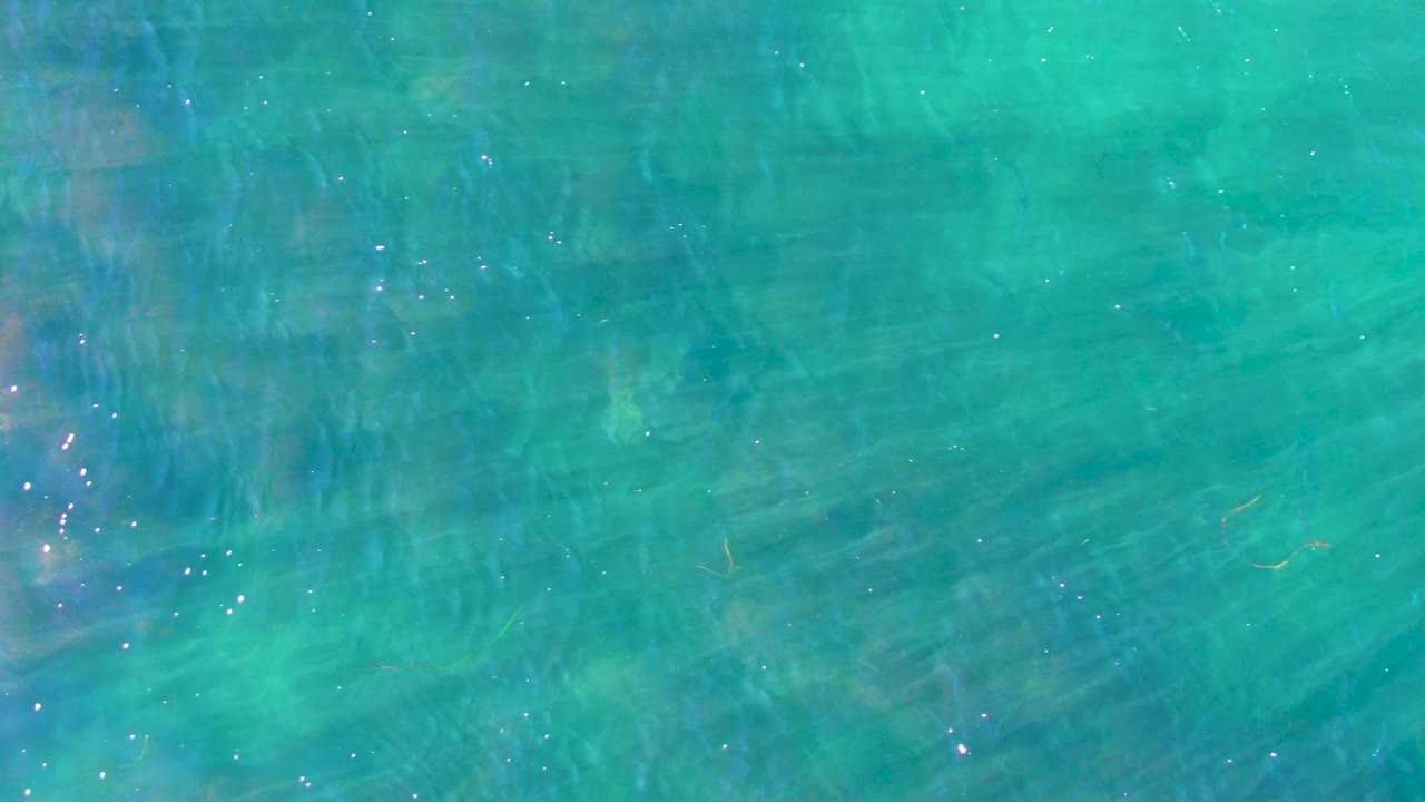 Transparent turquoise water in La Bocana, Baja California Sur, with a brighter cluster of sun reflections along one side and no visible people.