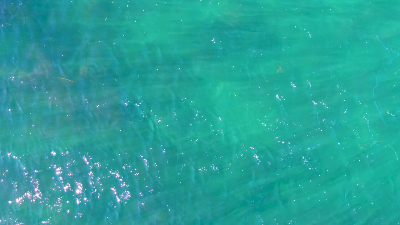 Transparent turquoise ocean water in La Bocana with soft darker underwater streaks, scattered white highlights, gentle ripple texture, and no visible people.