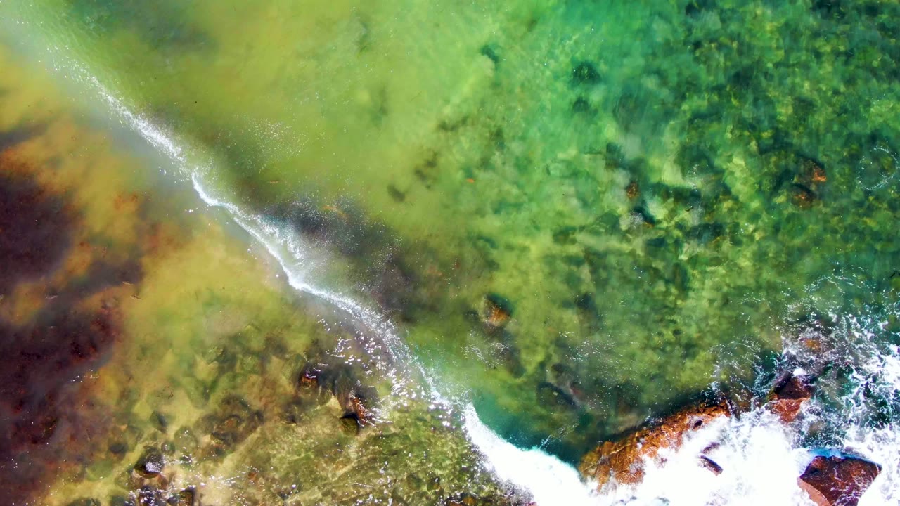 White foam crossing green water beside rocky shore