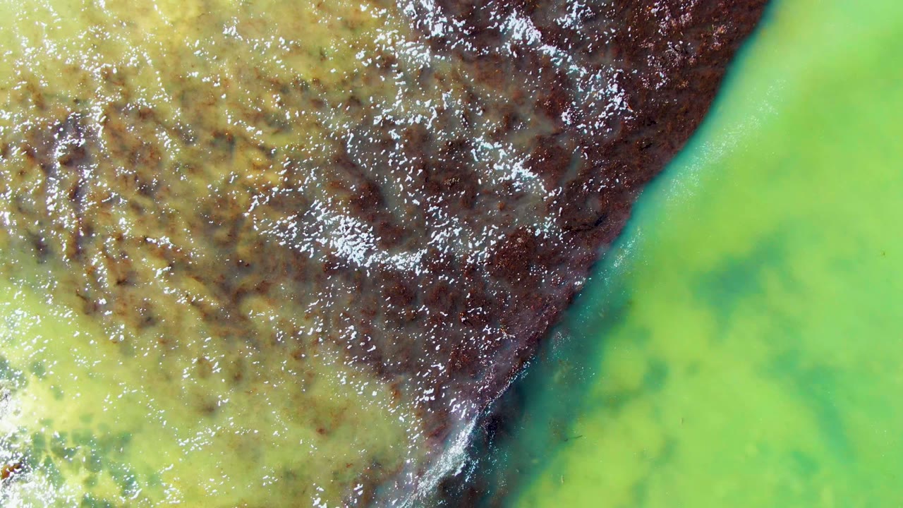Green water fills much of the frame while mottled yellow-brown water and a dark current edge occupy the upper right in La Bocana, Baja California Sur, with no visible people.