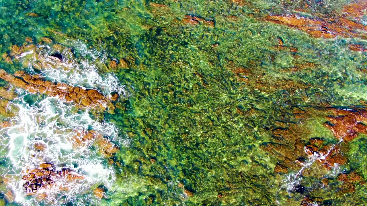 White foam spreading across rust-colored rocks underwater
