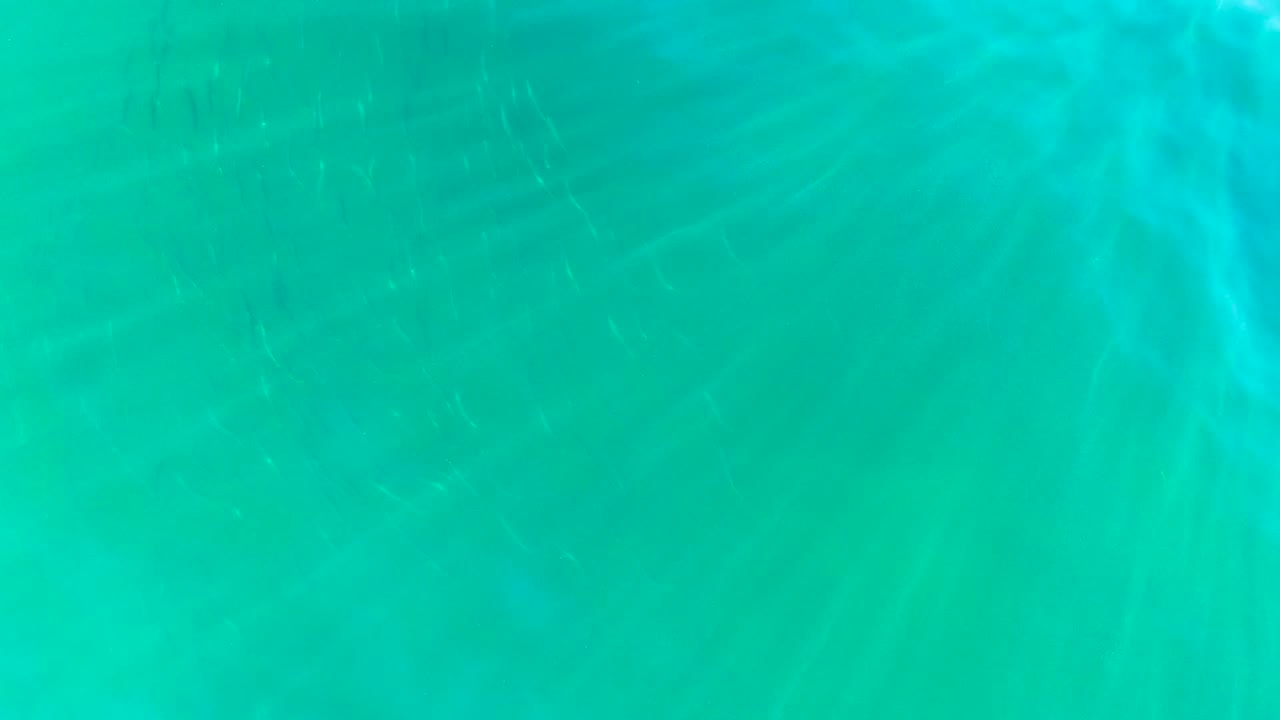Turquoise underwater view in La Bocana, Baja California Sur, with faint vertical sun rays near the surface and no visible people.